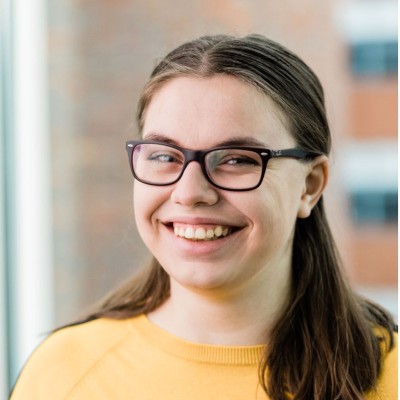 Portrait of Miriam Götz, smiling, in glasses and a yellow sweater