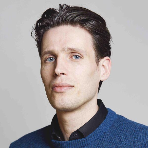Portrait of Mirre Simons in a blue sweater against a gray background